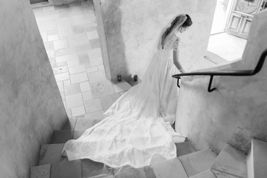 Bride Alyssa Campanella walks down a spiraling stone staircase at Sunstone Villa in her custom Lauren Elaine wedding gown and veil