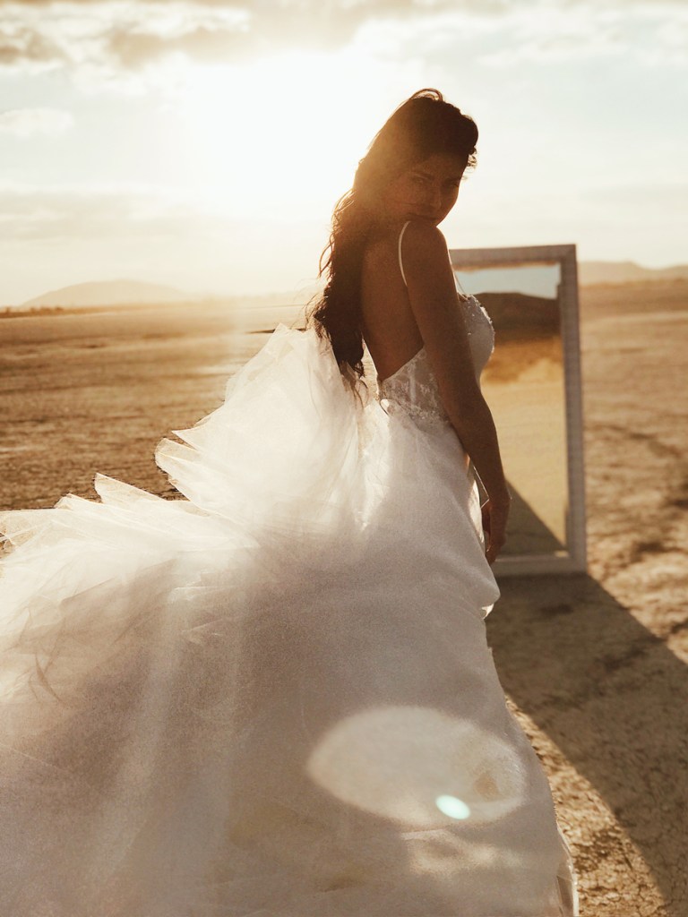 A model poses in front of a mirror at el mirage dry lake bed in California wearing a lauren elaine mermaid wedding dress