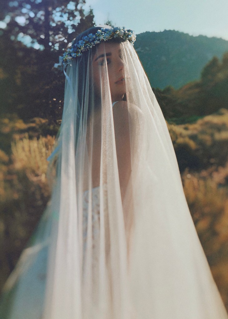 A model wears a Lauren Elaine blusher cathedral veil paired with flower crown for bohemian bridal fashion editorial.